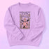 Comfort Colors garment-dyed sweatshirt featuring 'Patriarchy Slayer' design with pink armored knight holding sword and banner reading 'Burn It Down', surrounded by decorative floral border with roses and leaves. Made from 80% ring-spun cotton and 20% polyester with relaxed fit and rolled-forward shoulders. Available in lavender purple and seafoam green colorways, sizes S-3XL unisex, featuring sustainable made-to-order production with OEKO-TEX certified low-impact dyes and zero waste manufacturing process.